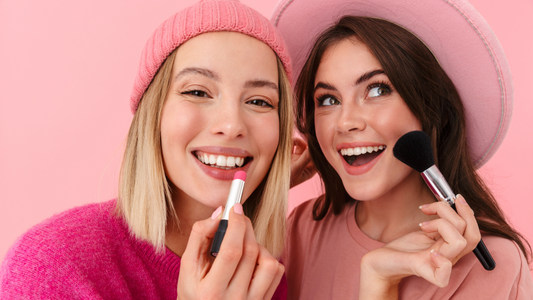 Dos chicas sonriendo y aplicándose pintalabios y colorete